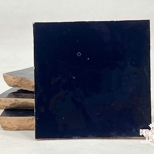 Pode incluir: Pilha de quatro azulejos de cerâmica azul escuro com uma superfície áspera e texturizada. Os azulejos são quadrados e têm uma borda ligeiramente irregular.