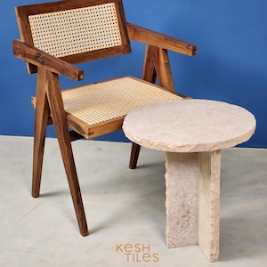 May include: A wooden chair with a woven cane seat and back, next to a round, light-colored stone side table. The chair and table are on a light gray floor. The text "Kesh Tiles" is visible in the lower right corner of the image.