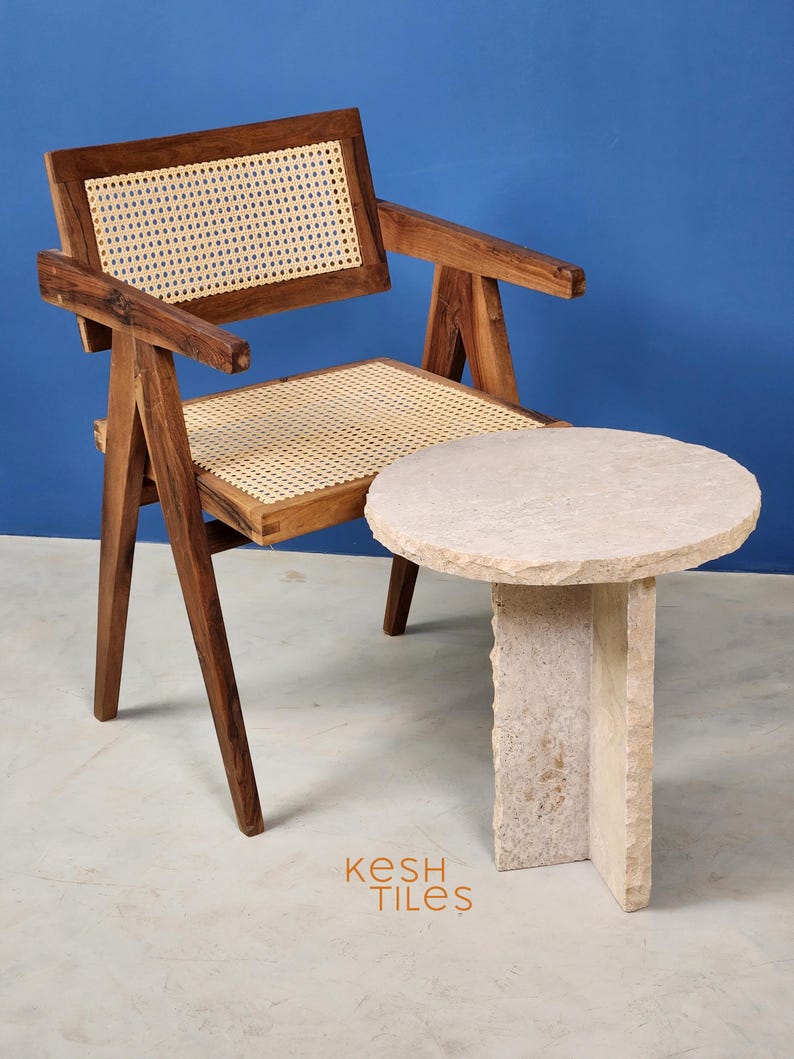 May include: A wooden chair with a woven cane seat and back, next to a round, light-colored stone side table. The chair and table are on a light gray floor. The text "Kesh Tiles" is visible in the lower right corner of the image.