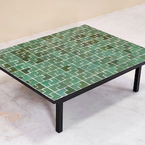May include: A rectangular coffee table with a green tile top and black legs. The tile design features a repeating geometric pattern in shades of green and white. The table is a low, modern design.