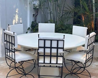 May include: A round white dining table paired with five chairs featuring black metal grid-patterned backrests and white seat cushions. The chairs have curved metal legs, and the table is supported by a central cylindrical white pedestal base.
