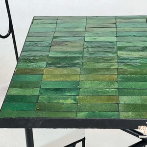 Pode incluir: Uma mesa com tampo de azulejos verdes e moldura de metal preto. Os azulejos est&atilde;o dispostos em forma de grade e t&ecirc;m um acabamento brilhante.