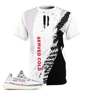 May include: White t-shirt with a black and white graphic design and the text "SERVED COLD" in red. A pair of white and black sneakers with red text are in the foreground. The shirt features a silhouette of a person.