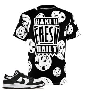 May include: Black and white graphic t-shirt with a panda pattern and the text "BAKED FRESH DAILY." A black and white sneaker with a white sole is next to the shirt. The shirt has a crew neck and short sleeves.