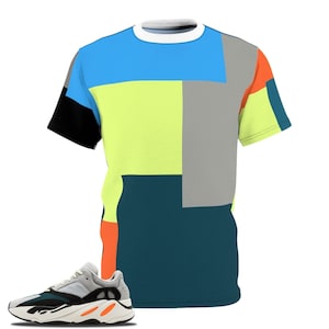 May include: A vibrant t-shirt featuring a geometric pattern in blue, yellow, grey, orange, and black. A pair of grey, black, and orange trainers is next to the shirt. The shirt has a white collar and short sleeves.