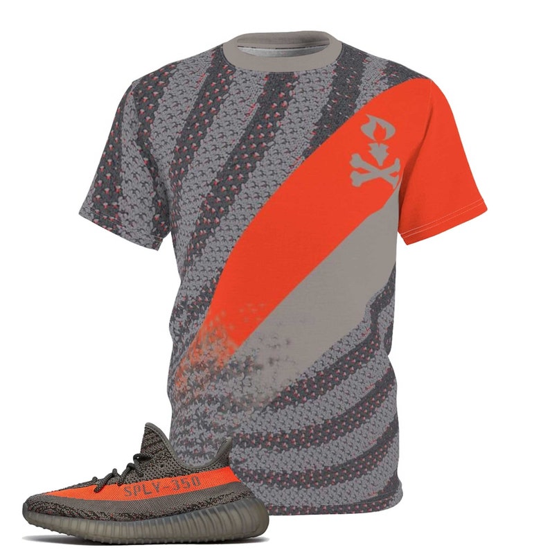 May include: A grey and orange graphic t-shirt with a diagonal stripe and a skull and crossbones design. A matching grey and orange trainer with the text "SPLY-350" is in the foreground. The shirt has a crew neck and short sleeves.