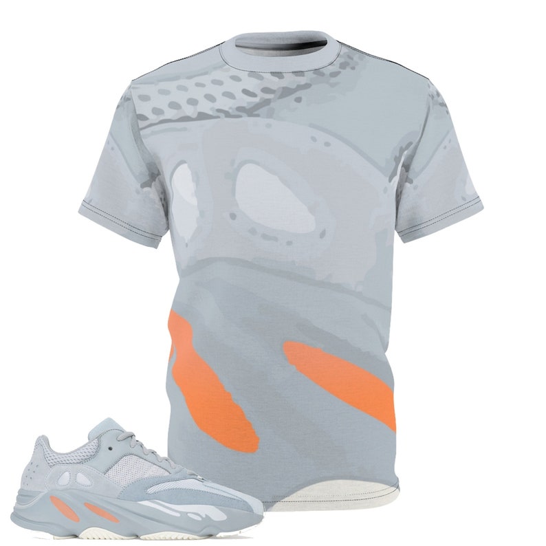 May include: A light gray t-shirt with an abstract design and orange accents, paired with a light gray and orange athletic shoe. The shoe features a mesh upper and a chunky sole, creating a modern, sporty look.