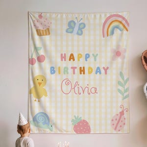 Könnte beinhalten: Eine Geburtstagsparty-Szene mit einem Hintergrund mit gelbem Vichy-Muster und farbenfrohen Illustrationen. Der Hintergrund lautet "Happy Birthday Olivia". Ein kleiner Kuchen mit brennenden Kerzen steht auf einem Tisch. Herzförmige Luftballons und ein Kind mit Partyhut sind ebenfalls zu sehen.