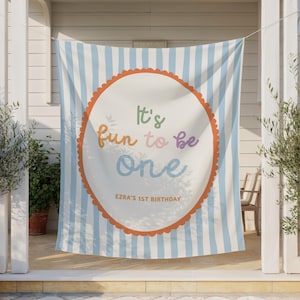 May include: A banner with a light blue and white striped background. A white circle with an orange scalloped border in the center features the text "It's fun to be one" in colorful letters. The text "Ezra's 1st Birthday" is below.