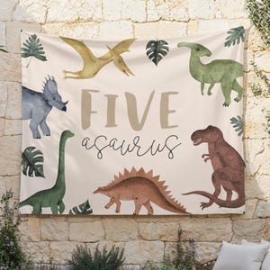 May include: A beige banner with the text "FIVEsaurus" in brown lettering. The banner features illustrations of various dinosaurs, including a green dinosaur, a brown dinosaur, a blue dinosaur, a yellow dinosaur, and a green dinosaur with a long neck.