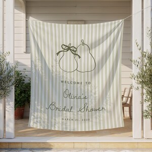May include: A striped fabric banner with a pear illustration and the text "Welcome to Olivia's Bridal Shower, March 21, 2028." The banner is light green and white, hanging between two white columns with potted plants on either side.