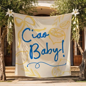 Puede incluir: Una pancarta color crema con las palabras "Ciao Baby!" en escritura azul, acentuada con ilustraciones de limones y lazos amarillos. La pancarta est&aacute; suspendida entre dos &aacute;rboles, decorada con flores blancas y vegetaci&oacute;n, frente a un edificio.