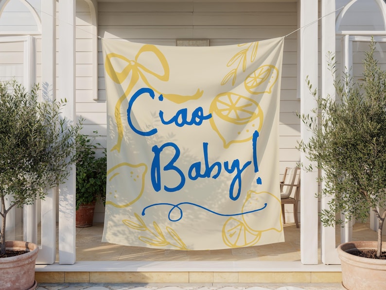 Puede incluir: Una pancarta color crema con las palabras "Ciao Baby!" en escritura azul. Ilustraciones de limones amarillos y un dise&ntilde;o de lazo rodean el texto. La pancarta est&aacute; colgada afuera, con olivos en macetas a ambos lados.