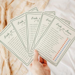 May include: A set of off-white paper game cards titled Bride or Groom with a scalloped border. Each card features a list of fifteen questions and two columns of small red and blue star icons for marking answers to the wedding-themed trivia game.
