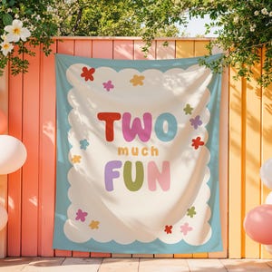 Puede incluir: Una pancarta con las palabras "TWO much FUN" en letras coloridas, rodeada por un borde festoneado y acentos florales. La pancarta se muestra contra un fondo de una pared rosa y naranja, con globos y flores.