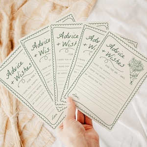 May include: A collection of cream-colored advice and wishes cards with green text and a scalloped border. The cards feature the text "Advice + Wishes" and prompts for the recipient to fill out. A bouquet illustration is on one card. The cards are held in a hand.