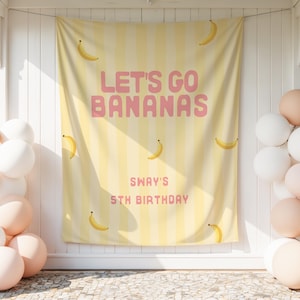 May include: A yellow and white striped fabric backdrop featuring a banana pattern and the pink text "LET'S GO BANANAS" followed by "SWAY'S 5TH BIRTHDAY". The backdrop is flanked by clusters of white and peach-colored balloons on both sides.