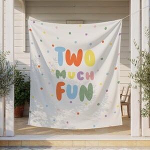 May include: A white banner with colorful polka dots and the words "TWO MUCH FUN" in large, playful letters. The text is in various colors, including blue, orange, yellow, purple, and green. The banner is hanging outdoors.