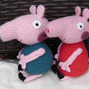 Könnte beinhalten: Zwei gehäkelte Schweine-Plüschtiere, eines in rosa und türkis, das andere in rosa und rot.