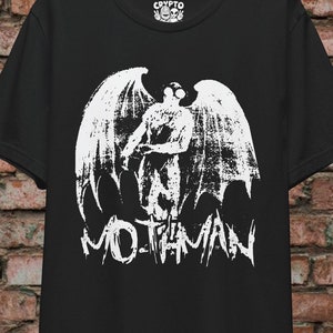 Könnte beinhalten: Schwarzes T-Shirt mit einem weißen Aufdruck einer geflügelten Kreatur mit dem Text "Mothman" darunter.