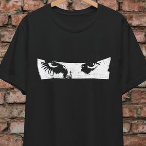 May include: Black t-shirt featuring a white graphic of a pair of eyes with long eyelashes.