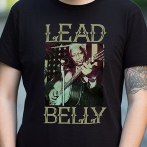May include: A black t-shirt with a vintage-style image of Lead Belly playing a guitar. The text "LEAD BELLY" is printed in a stylized font above the image.