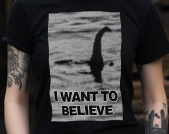 Może przedstawiać: Czarny T-shirt z grafiką stworzenia z Loch Ness, jeziora w Szkocji. Pod grafiką nadrukowany jest tekst "I WANT TO BELIEVE".