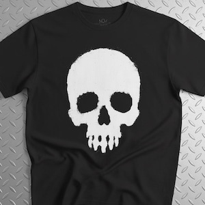 Könnte beinhalten: Ein schwarzes T-Shirt mit kurzen Ärmeln und einer großen, mittig platzierten weißen Grafik eines menschlichen Schädels. Das Schädeldesign hat ein strukturiertes, abgenutztes Aussehen mit leeren Augenhöhlen und Nasenöffnung auf der Brust.
