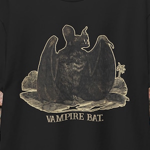 May include: A black t-shirt with a vintage illustration of a vampire bat in a gold color. The text "Vampire Bat." is printed below the image.
