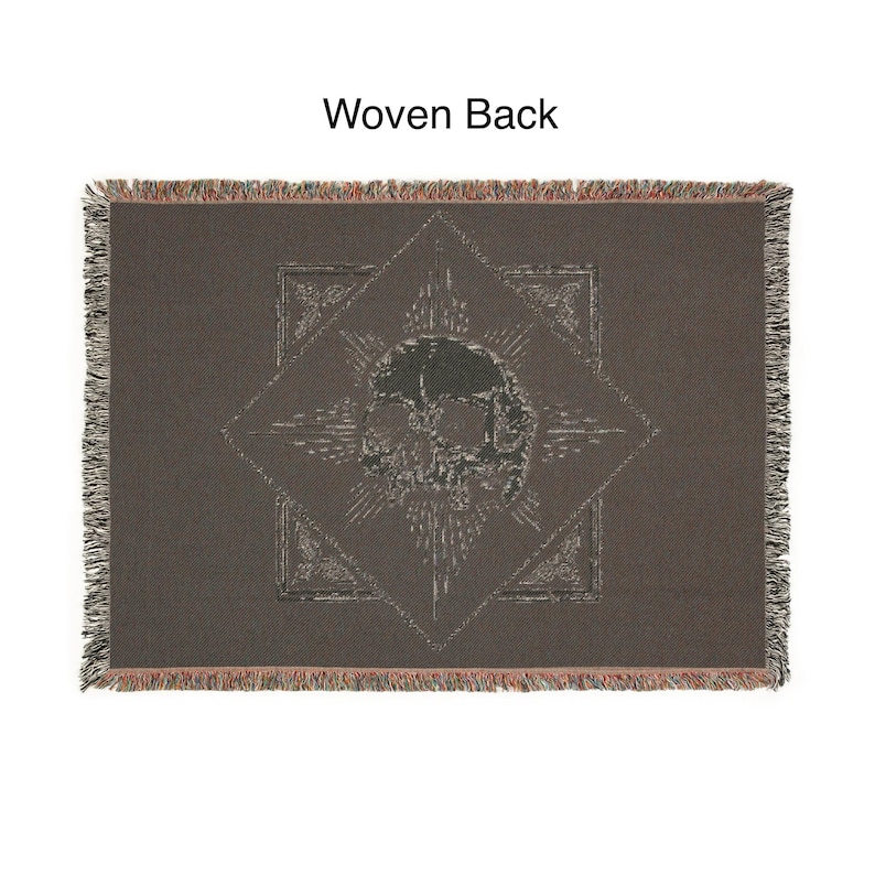 May include: A dark brown woven throw blanket with a skull design in the center. The skull is surrounded by a starburst pattern and geometric shapes. The blanket has a fringed edge and the text "Woven Back" at the top.