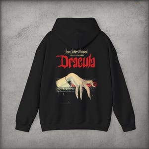 May include: A black hooded sweatshirt featuring a graphic print on the back. The text reads Bram Stoker's Original Dracula in red and white lettering. Below the text is an illustration of a pale hand with long fingernails resting on a dark edge.
