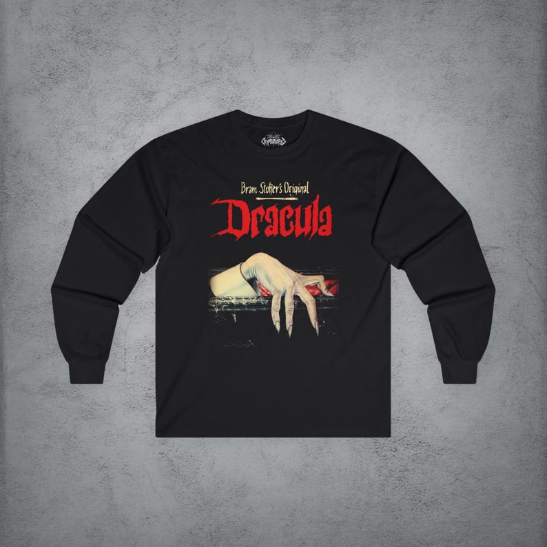 May include: A black long-sleeve t-shirt featuring the text Bram Stoker's Original Dracula in red and white lettering. Below the text is a graphic illustration of a pale, claw-like hand resting on a dark ledge with a red accent underneath.