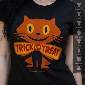 May include: A black t-shirt featuring a large, stylized orange cat graphic with yellow eyes and a wide smile. A prominent orange banner across the cat's chest displays the text TRICK OR TREAT in bold, dark orange capital letters.