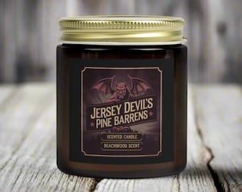 May include: A brown glass candle jar with a gold lid. The label features a black and white illustration of a gargoyle with the text "Jersey Devil's Pine Barrens" and "Beachwood Scent".