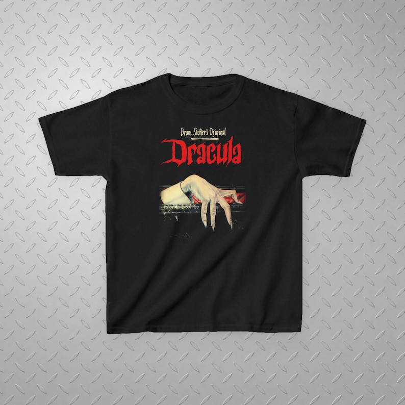 May include: A black short-sleeve t-shirt featuring a graphic print of a pale hand with long fingernails resting on a dark ledge. Above the hand, the text reads Bram Stoker's Original Dracula in a stylized red and white font on the chest.