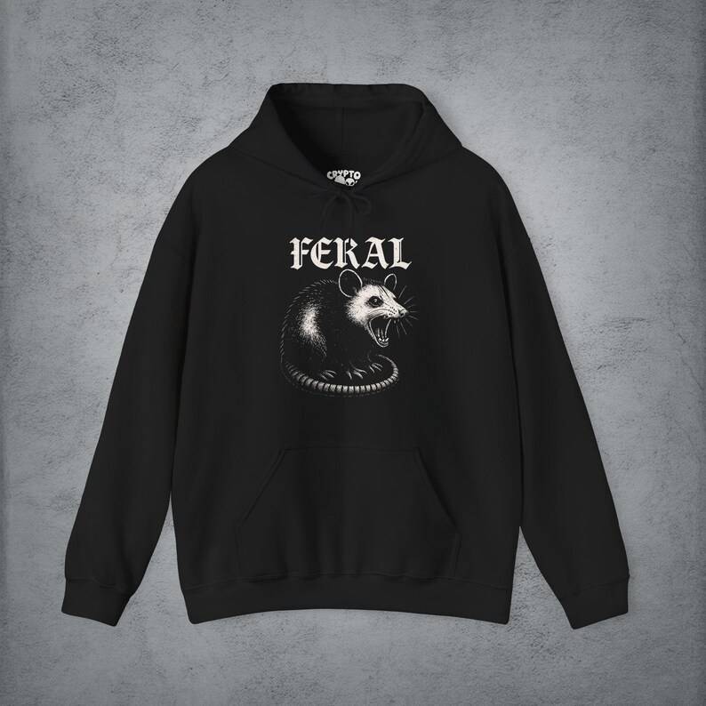 Puede incluir: Una sudadera con capucha negra que presenta un gr&aacute;fico blanco de una zarig&uuml;eya siseando centrado en el pecho. Sobre la zarig&uuml;eya, la palabra FERAL est&aacute; impresa en una fuente g&oacute;tica blanca. La prenda incluye un bolsillo canguro y mangas largas.