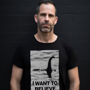 Model showcases a cryptozoology-inspired Loch Ness shirt, with a vivid depiction of Nessie and the phrase "I Want to Believe", blending intrigue and style for lake monster fans and mystery lovers.