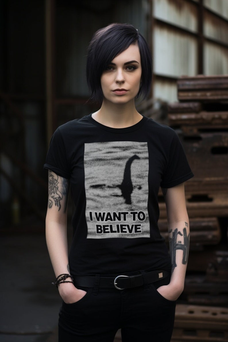 Model wearing a Loch Ness Monster believer T-shirt, featuring iconic "I Want to Believe" phrase with Nessie silhouette against a scenic lake background, perfect for fans of cryptozoology and unexplained mysteries.