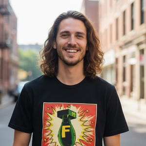Pode incluir: Uma pessoa sorrindo com cabelo castanho longo e ondulado usando uma camiseta preta. A camiseta apresenta um gr&aacute;fico colorido de uma bomba com a letra "F" em um fundo vermelho e amarelo. O fundo &eacute; uma rua da cidade.