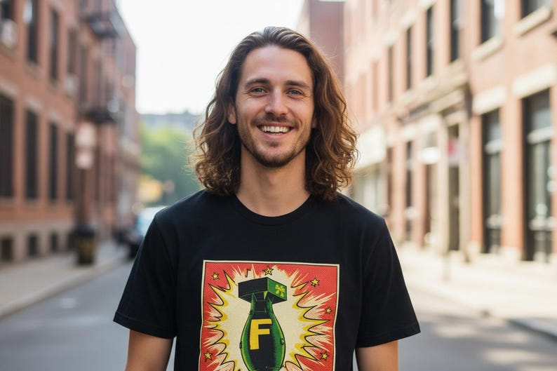 Pode incluir: Uma pessoa sorrindo com cabelo castanho longo e ondulado usando uma camiseta preta. A camiseta apresenta um gr&aacute;fico colorido de uma bomba com a letra "F" em um fundo vermelho e amarelo. O fundo &eacute; uma rua da cidade.