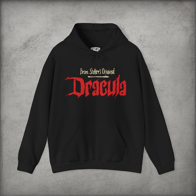 May include: A black hooded sweatshirt featuring a front graphic with the text Bram Stoker's Original in white and the word Dracula in a large, jagged red font. The garment includes a drawstring hood and a large front kangaroo pocket.