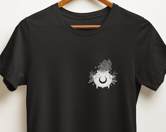 May include: Black t-shirt with a white graphic of a cauldron with a crescent moon and floral accents.