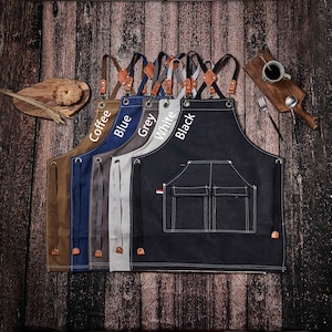May include: A set of 6 canvas aprons in different colors, including coffee, blue, grey, white, and black. Each apron has adjustable straps and two pockets. The aprons are lined up in a row, with the straps facing the viewer.