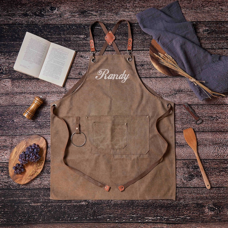May include: Brown canvas apron with adjustable straps and a large pocket. The apron has the name "Randy" embroidered on the front in white thread.