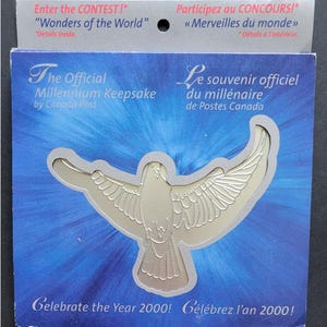 Puede incluir: Una paloma plateada con las alas extendidas, una reliquia conmemorativa para el año 2000. El texto "The Official Millennium Keepsake by Canada Post" está impreso en la tarjeta. El texto "Celebrate the Year 2000!" está impreso en la parte inferior de la tarjeta.
