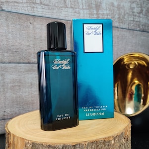 Könnte beinhalten: Eine blaue Glasflasche mit Davidoff Cool Water Eau de Toilette. Die Flasche steht auf einer Holzoberfläche. Die Flasche enthält 75 ml (2,5 fl oz).