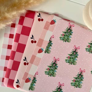 Peut inclure: Quatre feuilles de papier à motifs roses et rouges sur fond de pois blancs. Les motifs comprennent un vichy rouge et blanc, un vichy rose et blanc, un motif rose et blanc avec des fraises et des cerises, et un motif rose avec des sapins de Noël et des nœuds.
