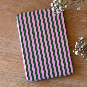 Peut inclure: Un étui rectangulaire à rayures roses et vertes. Les rayures sont verticales et régulières. L'étui est posé sur une surface en bois, avec de petites fleurs blanches en arrière-plan.
