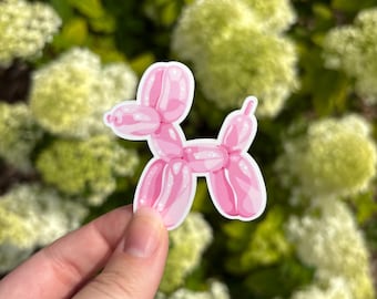 May include: A die-cut sticker featuring a light pink balloon animal shaped like a dog. The design includes white highlights to mimic the reflective surface of a balloon, with a distinct white border outlining the entire shape of the animal.