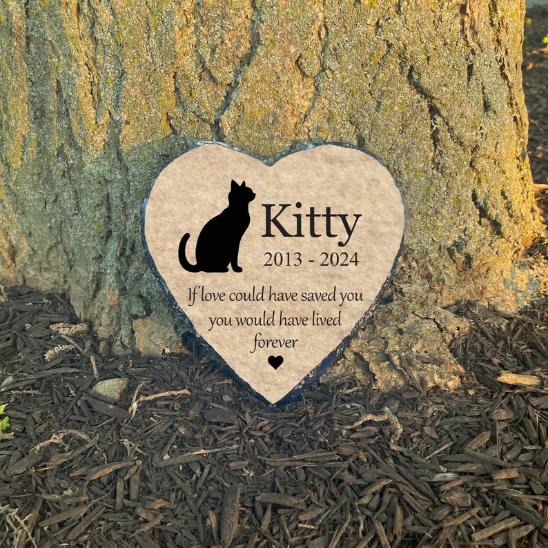 May include: Heart-shaped memorial stone featuring a black cat silhouette and the name "Kitty" with dates 2013-2024. The inscription reads, "If love could have saved you, you would have lived forever." A small heart symbol is at the bottom.